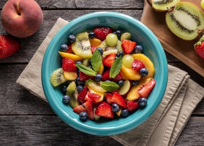 Fruktig fruktsalat med bær, kiwi og mango i en blå bolle, perfekt for kaker og dessert.